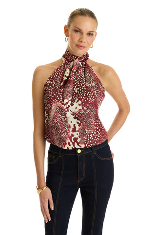 A woman poses against a white background wearing the Rina Tie Neck Blouse in Garnet Crush, paired with dark high-waisted jeans, gold hoop earrings, a gold bracelet, and her hair pulled back.