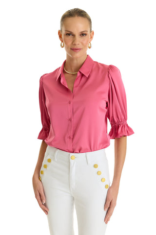 A woman wears the Cindy Ruffle Sleeve Shirt - Petal Pink with puff sleeves and high-waisted white pants with gold buttons, standing against a white background and smiling slightly.