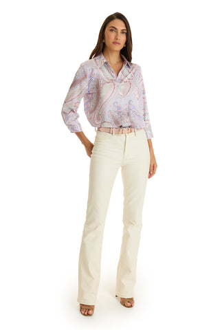 A woman faces forward against a white background, wearing the Sara Silk Blouse in pastel paisley with rolled sleeves, cream flared pants, a light pink belt, and beige open-toe heels.
