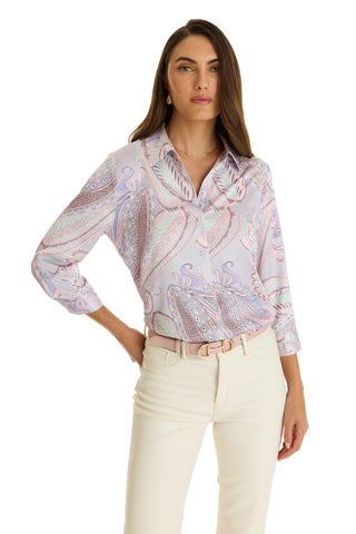 A woman stands confidently with one hand on her hip, wearing the Sara Silk Blouse - Pastel Paisley, tucked into high-waisted cream pants with a light pink belt.