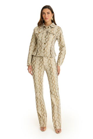A woman faces forward in the Bethanie Denim Jacket - Gold Python and matching flared pants with open-toe heels, set against a plain white background.