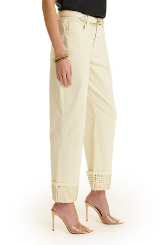 A person wearing the Ren Cropped Cuff Jean - Gold Mirror, featuring four-way stretch denim and gold-studded cuffs, paired with a black top, gold bracelets, and clear heels. The image is cropped below the shoulders.