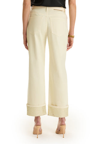 A person wearing the Ren Cropped Cuff Jean - Gold Mirror, featuring cream four-way stretch denim with large gold mirror studded hems, paired with nude heels. The back view highlights the pockets and a black top.