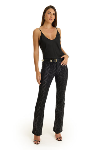A woman in slim bootcut black pants and a tank top, styled with the sleek look of Aria Flare Jean - Black Python.