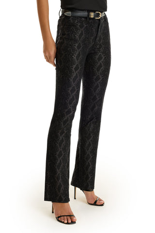 A person wearing black Aria Flare Jean - Black Python, a matching black belt, and black open-toe high heels, standing against a white background.