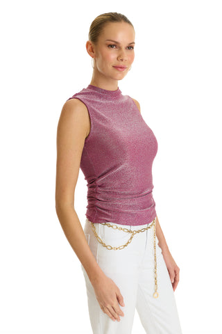 A woman models the Mia Shimmer Tank in amethyst, styled sleeveless with white pants and a gold chain belt, standing against a white background and smiling gently to the side.