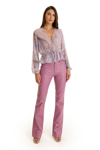 A woman faces forward in a Whitney Chiffon Top - Pastel Paisley, paired with high-waisted flared light purple pants and open-toe heels, set against a white background.