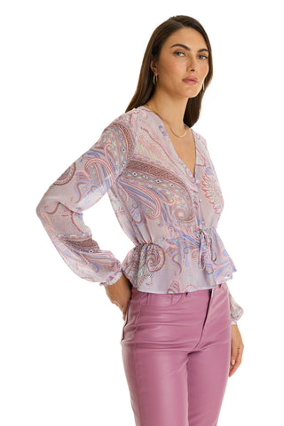 A woman stands confidently with one hand on her hip, wearing the Whitney Chiffon Top - Pastel Paisley and mauve high-waisted pants, against a white background.