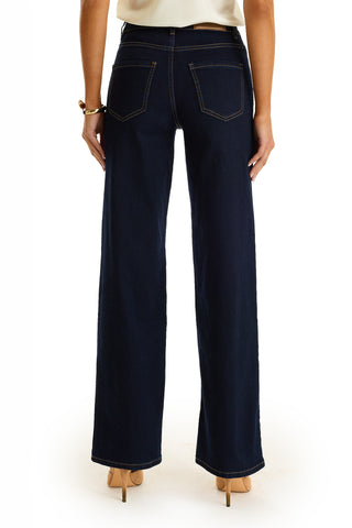 A person is shown from the back wearing the Kaia Studded High Rise Jean in Indigo with floral stitching and nude heels, standing against a plain white background.