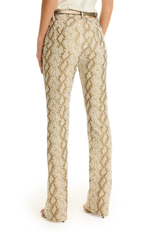 A person stands facing away, wearing Aria Flare Jean - Gold Python featuring a fitted waist, straight legs, back pockets, and a slim bootcut style that highlights the lower back and legs. Only these features are visible.