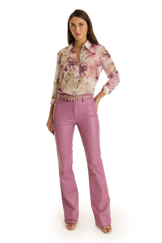 A woman with long, straight hair stands against a white background in a floral long-sleeve blouse and the Aria Coated Flare Jean - Mauve, featuring a high-rise slim fit and flared legs. She completes her look with open-toe heels.