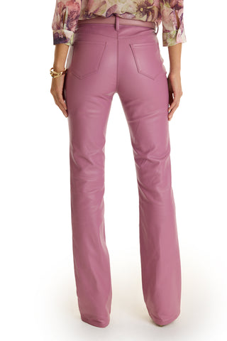 A person faces away, wearing high-rise Aria Coated Flare Jean in mauve with back pockets and a slim bootcut, paired with a floral long-sleeve blouse and a gold bracelet on their left wrist.