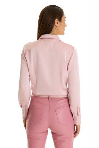 A woman with long brown hair, wearing the Paulina Silk Blouse in mauve and high-waisted pink pants, stands facing away from the camera against a white background.