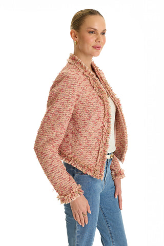 A woman in profile stands against a white background wearing the Florence Tweed Jacket - Rose Multi, featuring fringe hem and frayed edges, layered over a white top and blue jeans.