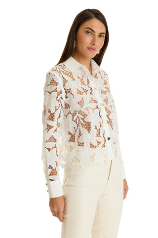 A woman wears the Mina Lace Blouse in white, featuring long sleeves, floral lace details, and white cuffs, paired with white pants against a plain white background.