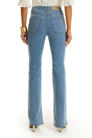 Someone is shown from the back wearing the Allegra Bootcut Jean in Medium Blue paired with a white top, gold bracelet on their left wrist, and high-heeled shoes.