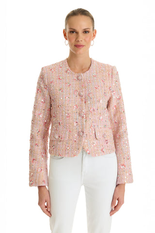 A woman faces forward, smiling softly with her hair pulled back, wearing the May Tweed Crystal Jacket in Pink Multi featuring sequined florals and diamond buttons, paired with white pants against a white background.