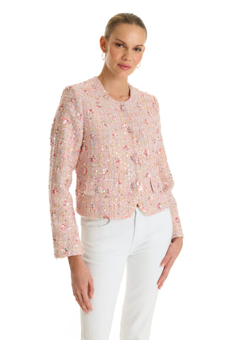 A woman stands against a white background wearing the May Tweed Crystal Jacket in Pink Multi with diamond button closure and white pants. Her hair is pulled back, she smiles slightly, and has one hand in her pocket.
