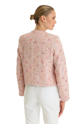 A woman with blonde hair in a low bun wears the May Tweed Crystal Jacket in Pink Multi and white pants, facing away and glancing to the side against a white background.