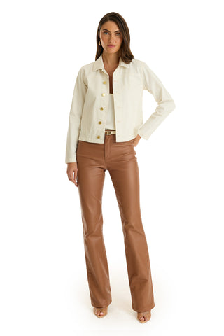 A woman faces forward in the Joelle Jean Jacket - Ivory, a white top, high-waisted brown leather flared pants, and tan heeled sandals, set against a plain white background.