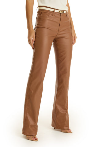 A woman wears the Aria Coated Flare Jean in Mocha, featuring a high-rise fit and subtle flare, styled with a cream belt and open-toe heels, standing against a white background.