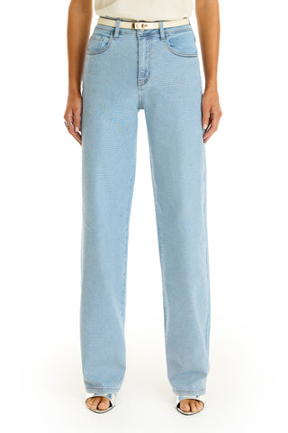 A person wearing medium blue, high-waisted Brynn Crystal Jean with a subtle dotted pattern, a white belt, and open-toe sandals stands against a white background.