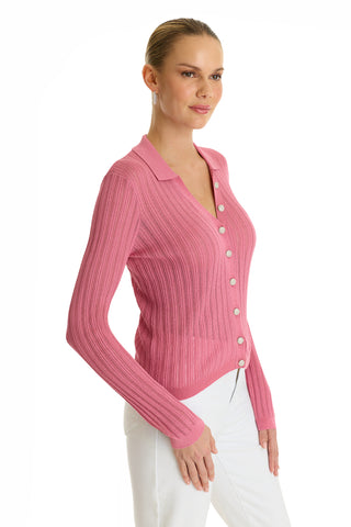 A woman with blonde hair in a low bun wears the Karolina Polo Shirt in Petal Pink with white pants, standing against a white background and smiling slightly.