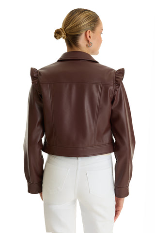 A woman with blonde hair in a low bun, silver hoop earrings, and white pants wears the Chantal Ruffle Sleeve Leather Jacket in Espresso, standing with her back to the camera against a white background.