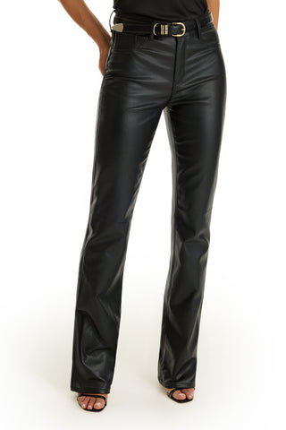 Someone wears high-waisted, black Aria Coated Flare Jeans with a belt and open-toe heels, standing against a white background. Only the pants and lower body are visible; the upper body is out of frame.
