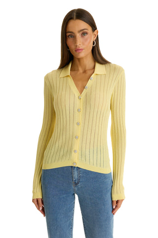 A woman wears the Karolina Polo Shirt in Sunshine Yellow, a ribbed lightweight knitwear button-up with collar and long sleeves, paired with blue jeans, standing against a plain white background.