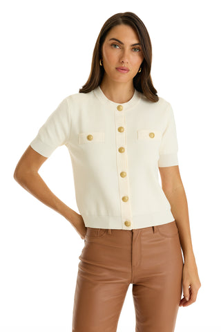 A woman wearing the Bonnie Knit Cardigan Top in Pearl, a short-sleeve cream knit with gold buttons, and brown high-waisted pants poses with one hand on her hip against a plain white background.