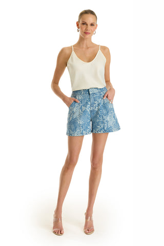 A woman stands against a white background wearing the Beverly Pleated Short in Crystal Snake print, a white sleeveless top, clear heeled sandals, hoop earrings, and her hair pulled back.