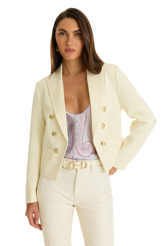 A woman poses with one hand on her hip against a white background, wearing the Gabrielle Double Breasted Blazer - Pearl with gold buttons, paired with a paisley-patterned top and matching cream pants.