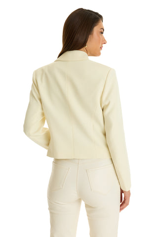 A woman stands with her back to the camera, head turned slightly, wearing the Gabrielle Double Breasted Blazer - Pearl and matching pants. The fitted, off-white ensemble looks chic and sophisticated against a plain white background.