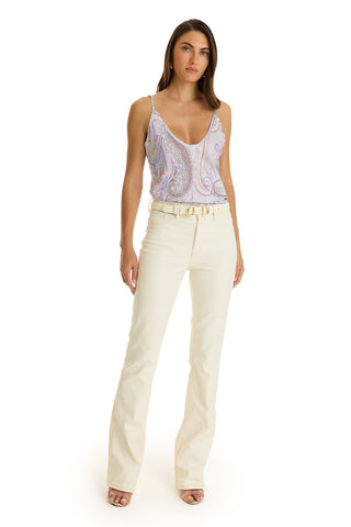 A woman faces forward against a plain white background, wearing the Yara Silk Camisole in pastel paisley with a deep v-neck, high-waisted white flared pants with a belt, and open-toe heels.