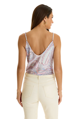 A woman with long brown hair and gold hoop earrings models the Yara Silk Camisole in Pastel Paisley, featuring a low back, paired with high-waisted cream pants, standing against a white background and facing away from the camera.