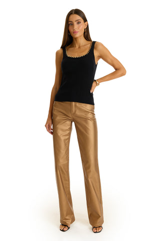 A woman with long hair stands against a white background wearing the Millie Knit Tank in black, paired with high-waisted gold wide-leg pants, black open-toe heels, earrings, and a bracelet.