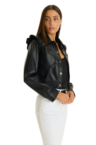 A woman with long brown hair models the Chantal Ruffle Sleeve Leather Jacket in black over a black top and white pants, posing against a white background and looking to her left.