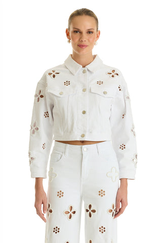 A woman wears the Kaia Pearl Jean Jacket in white, featuring cut-out flower patterns. She stands facing forward against a plain white background, smiling slightly.