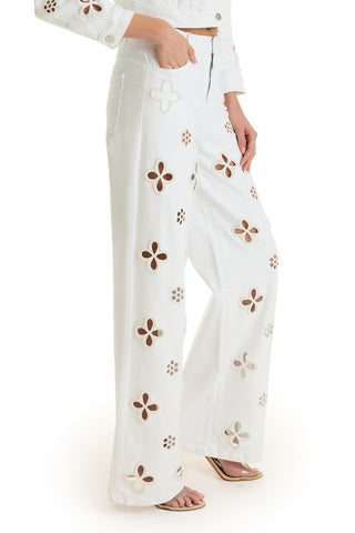 Someone wearing the Kaia Pearl High Rise Jean in White, featuring a high waist and large cutout flower designs. The straight-leg pants are paired with sandals, and a matching cropped jacket is partially visible.