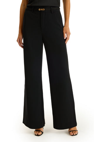A person wears the Martina Belted Trouser - Black, a tailored high-rise pant with a built-in belt and loose, flared legs, paired with open-toe heels. The image is cropped from shoulders down.