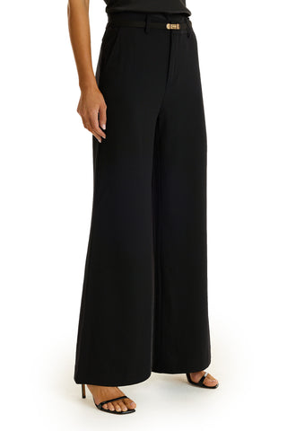 A person wearing the Martina Belted Trouser in black, featuring a high-rise and wide-leg design, paired with black open-toe heeled sandals, standing on a white background.