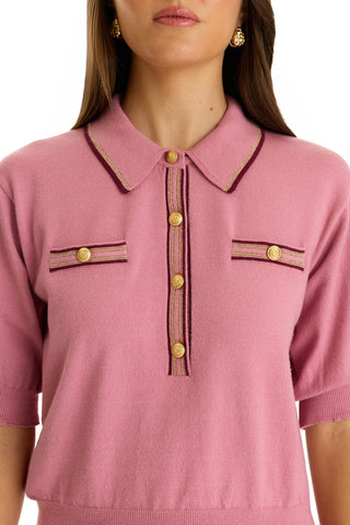 A woman wears the Bobbi Polo Shirt - Dusty Rose, an ultra-soft knit with short sleeves, a collar, gold buttons, and decorative pocket flaps. Gold earrings complete her elevated casual look as her face is partially visible.