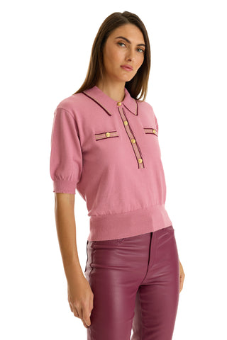 A woman wears the Bobbi Polo Shirt in Dusty Rose—an ultra-soft knit with short sleeves, collar, buttoned front, and two chest pockets—paired with high-waisted burgundy leather pants against a white background.