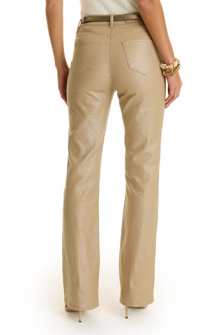 Woman facing away, wearing Aria Coated Flare Jean in Champagne—a high-rise, beige, flare-fit pant with back pockets and a tan belt—paired with a white sleeveless top and gold bracelets on a white background.