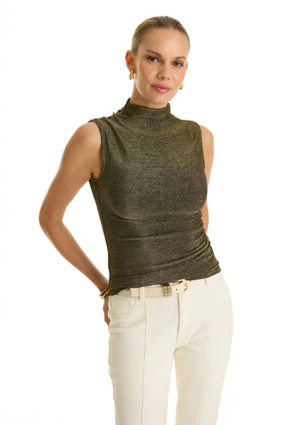 A person stands against a white background, wearing the Mia Shimmer Tank - Gold with a mock neckline and high-waisted belted white pants. Their hair is pulled back, accessorized with gold earrings and bracelets.
