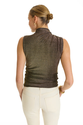 A woman with blonde hair in a sleek bun is seen from the back, wearing the Mia Shimmer Tank - Gold and high-waisted light beige pants. She accessorizes with hoop earrings and a bracelet against a plain white background.