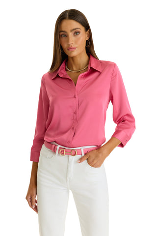 A woman poses confidently with one hand in her pocket, wearing the Sara Silk Blouse in Petal Pink, styled with white pants and a matching pink belt against a plain white background.