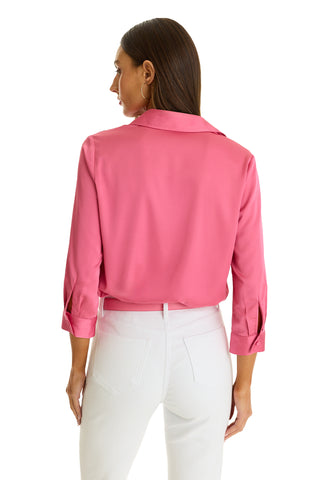 A woman with straight brown hair faces away, wearing the Sara Silk Blouse in Petal Pink with three-quarter sleeves and rolled cuffs, paired with white pants against a plain white background.