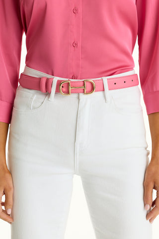 A person wears a bright pink button-up shirt tucked into high-waisted white jeans, accessorized with the Bettie Belt in Petal Pink—a pebbled faux leather belt featuring a gold-toned buckle.